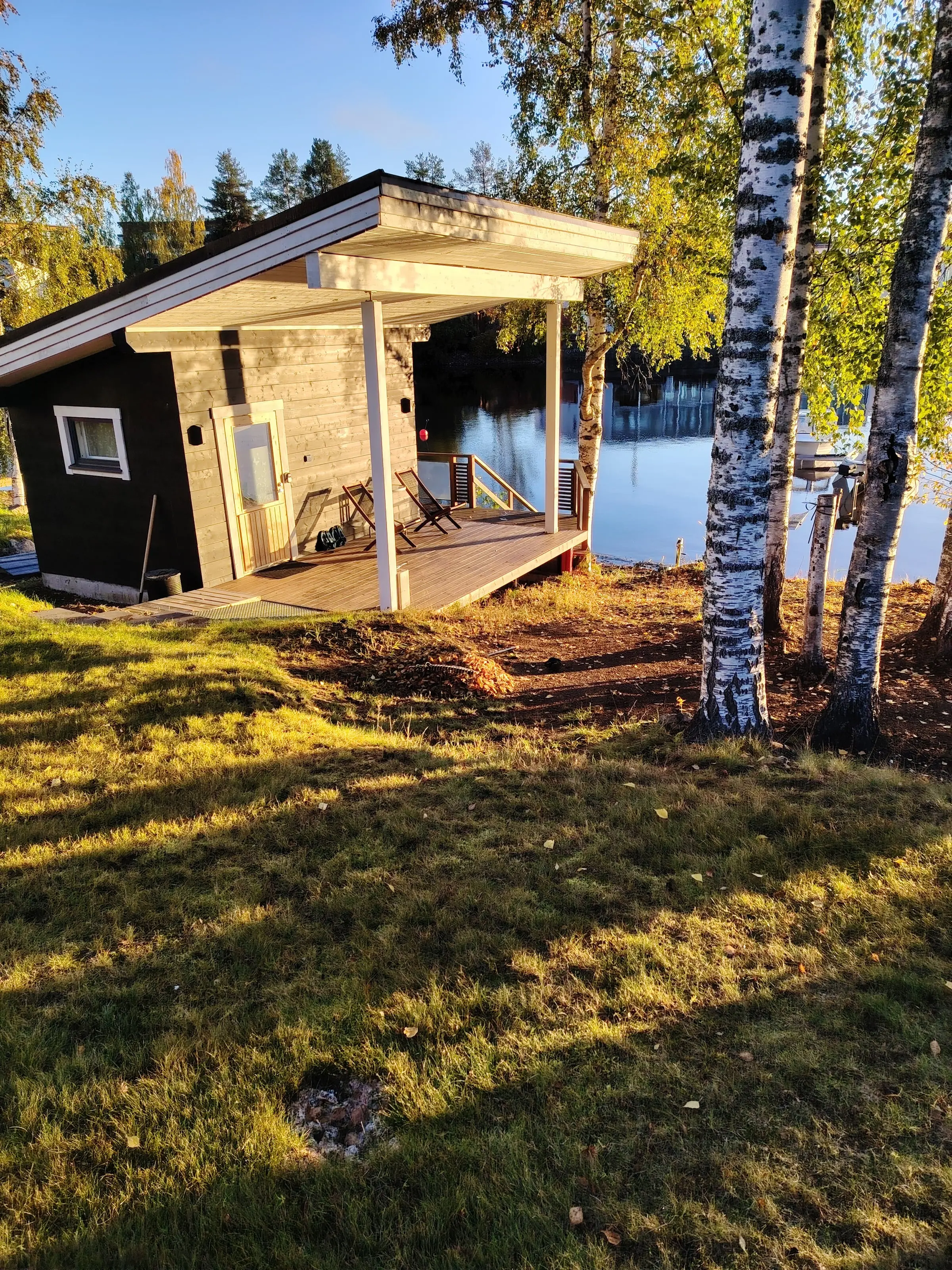 Rantasauna's covered terrace with two deck chairs, the lake just beyond the birch trees.