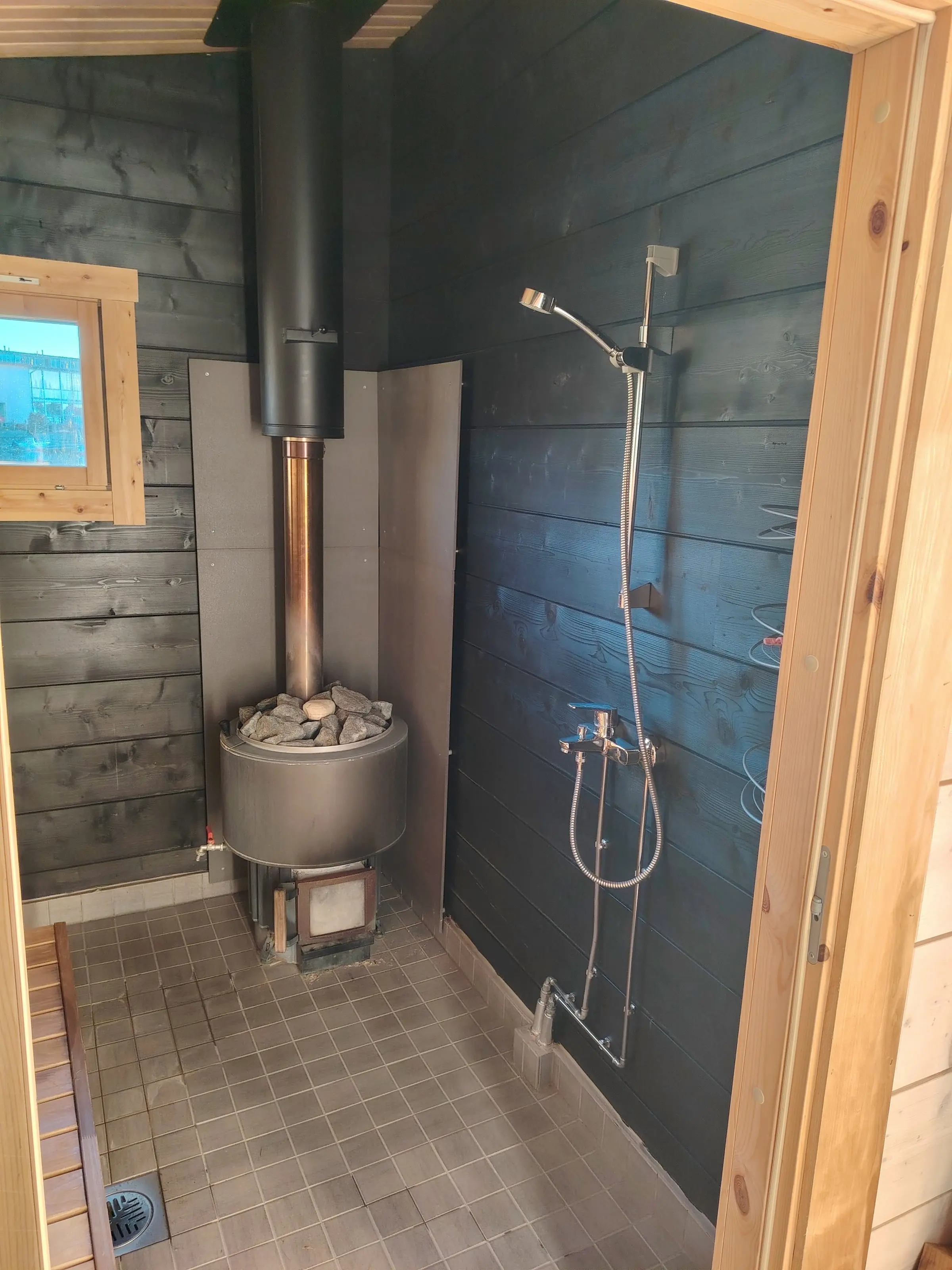 A shower on the wall beside the wood-burning stove in the sauna room.