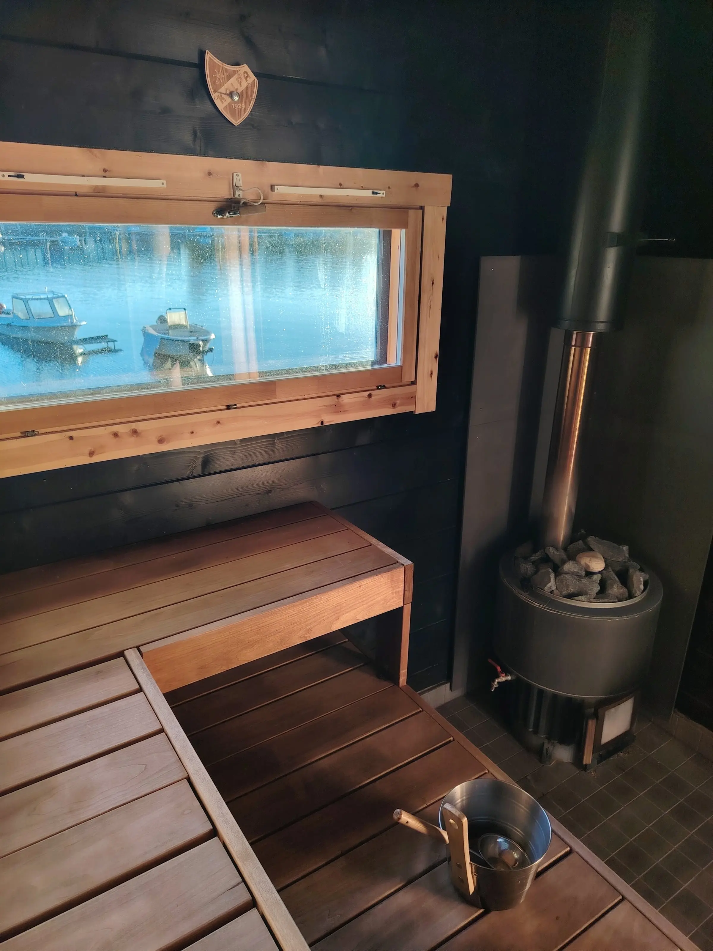 Sauna benches, the wood-burning stove and a wide window onto the lake with moored boats.
