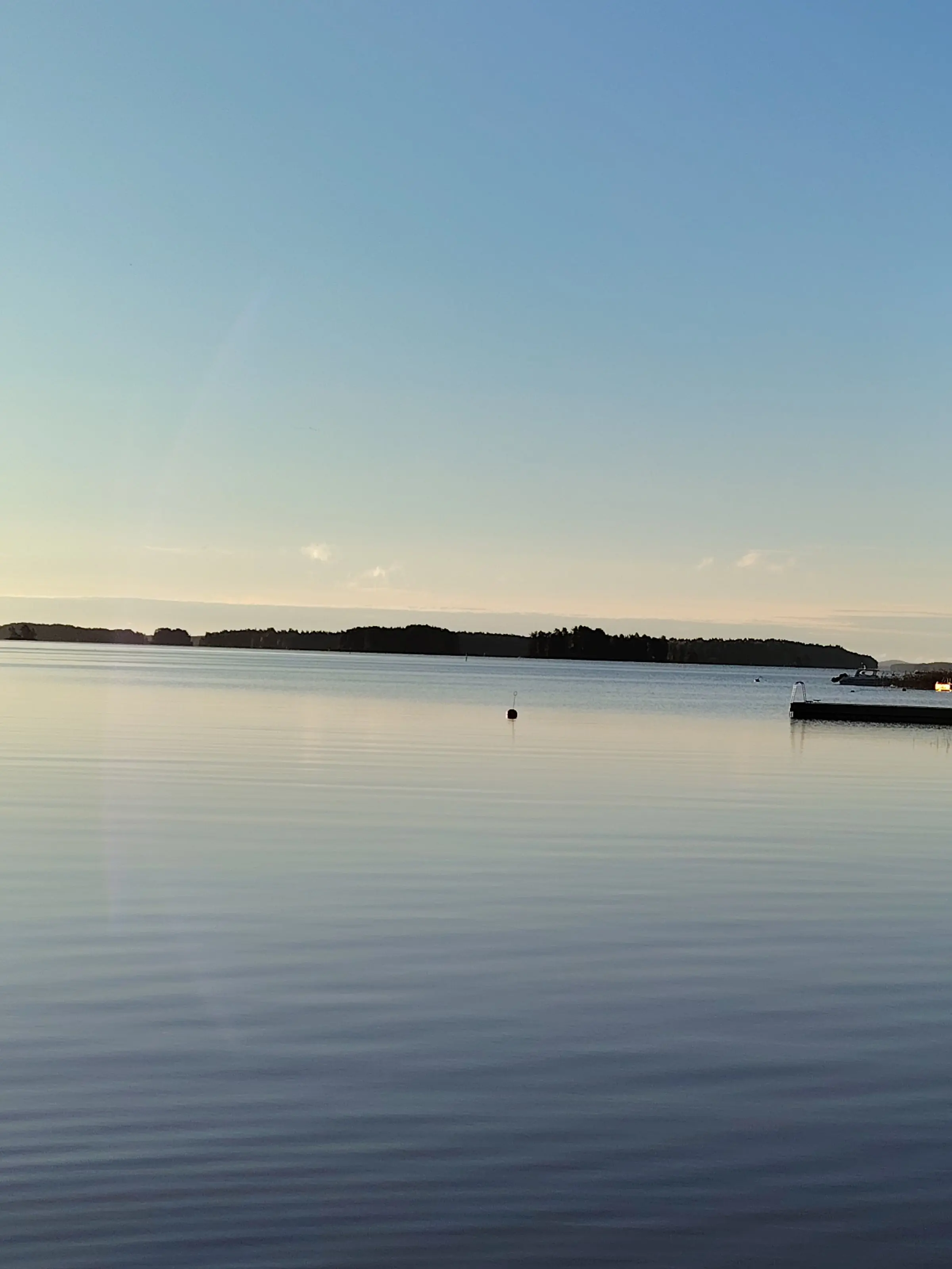 Tyyni järvi varhain aamulla, metsäinen rantaviiva horisontissa ja laituri oikealla.