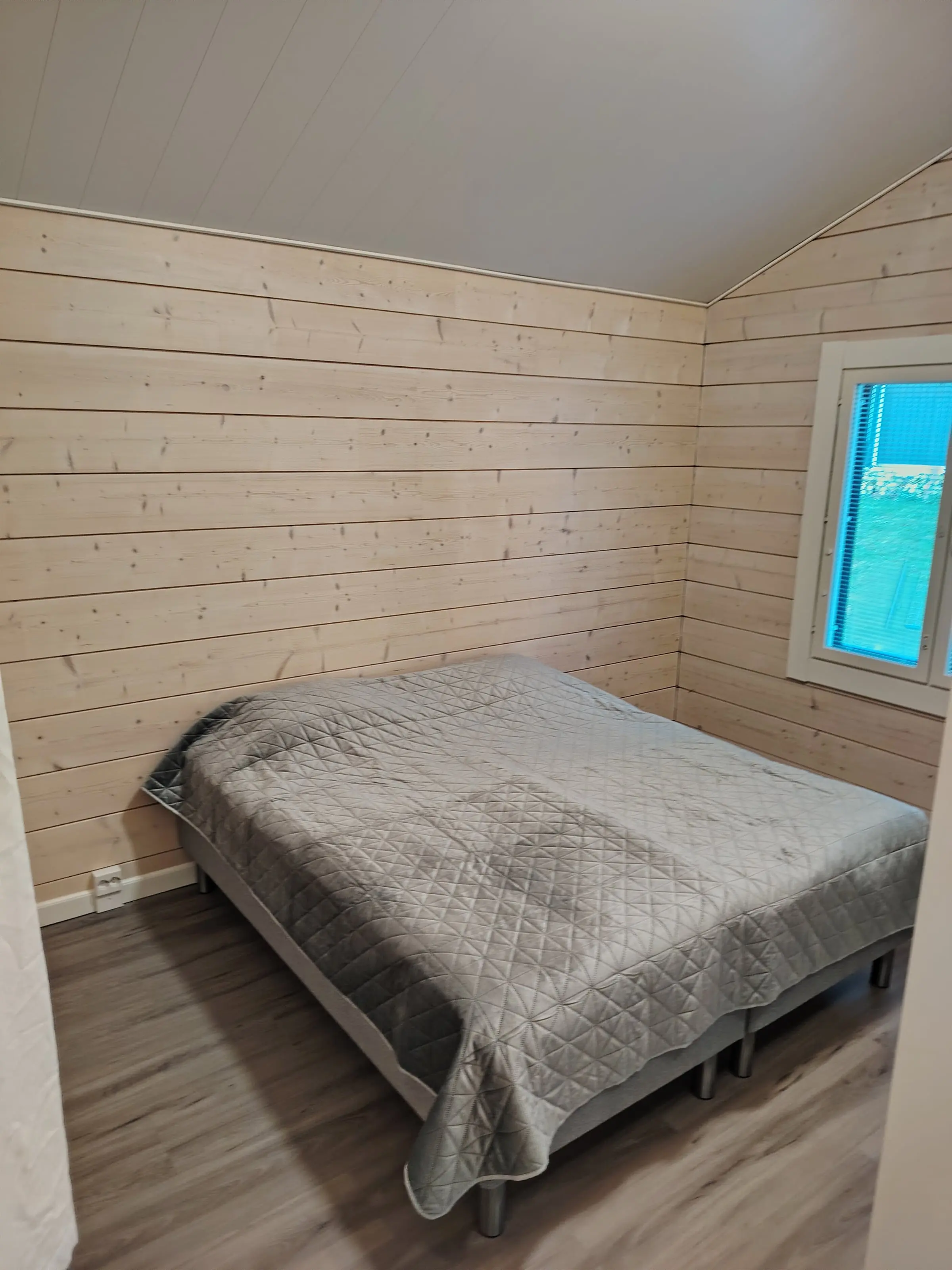 A bedroom with a double bed and light wood-panelled walls.